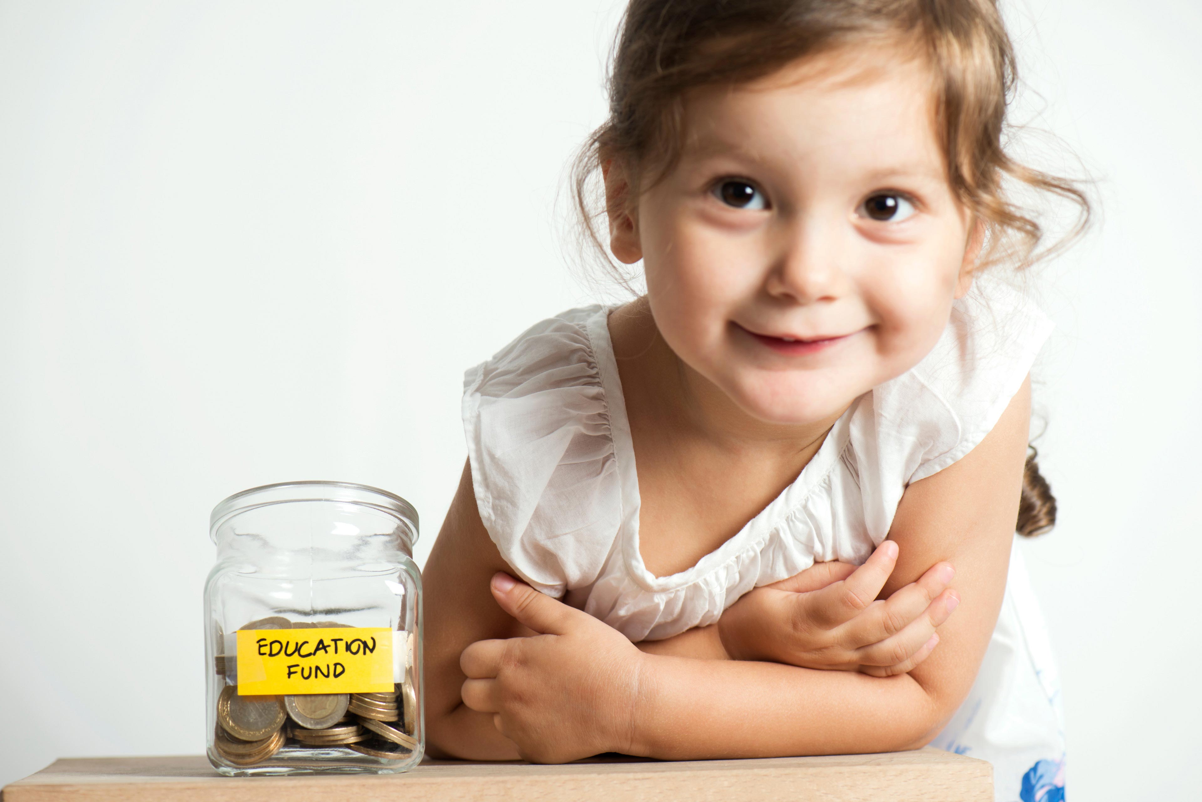 Little girl with coins in glass money jar with education fund label