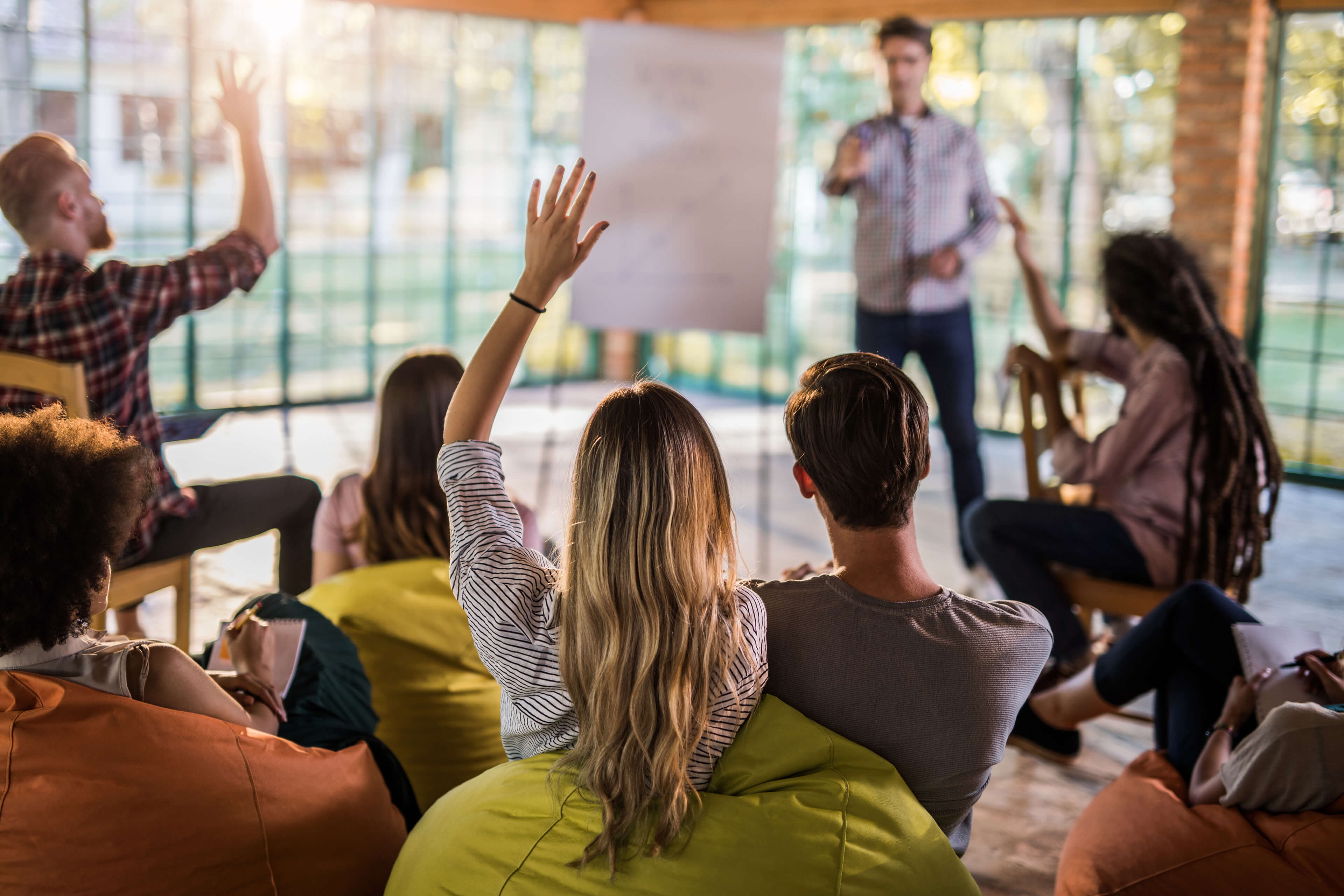 Woman raising hand at company meeting with participants on bean bags
